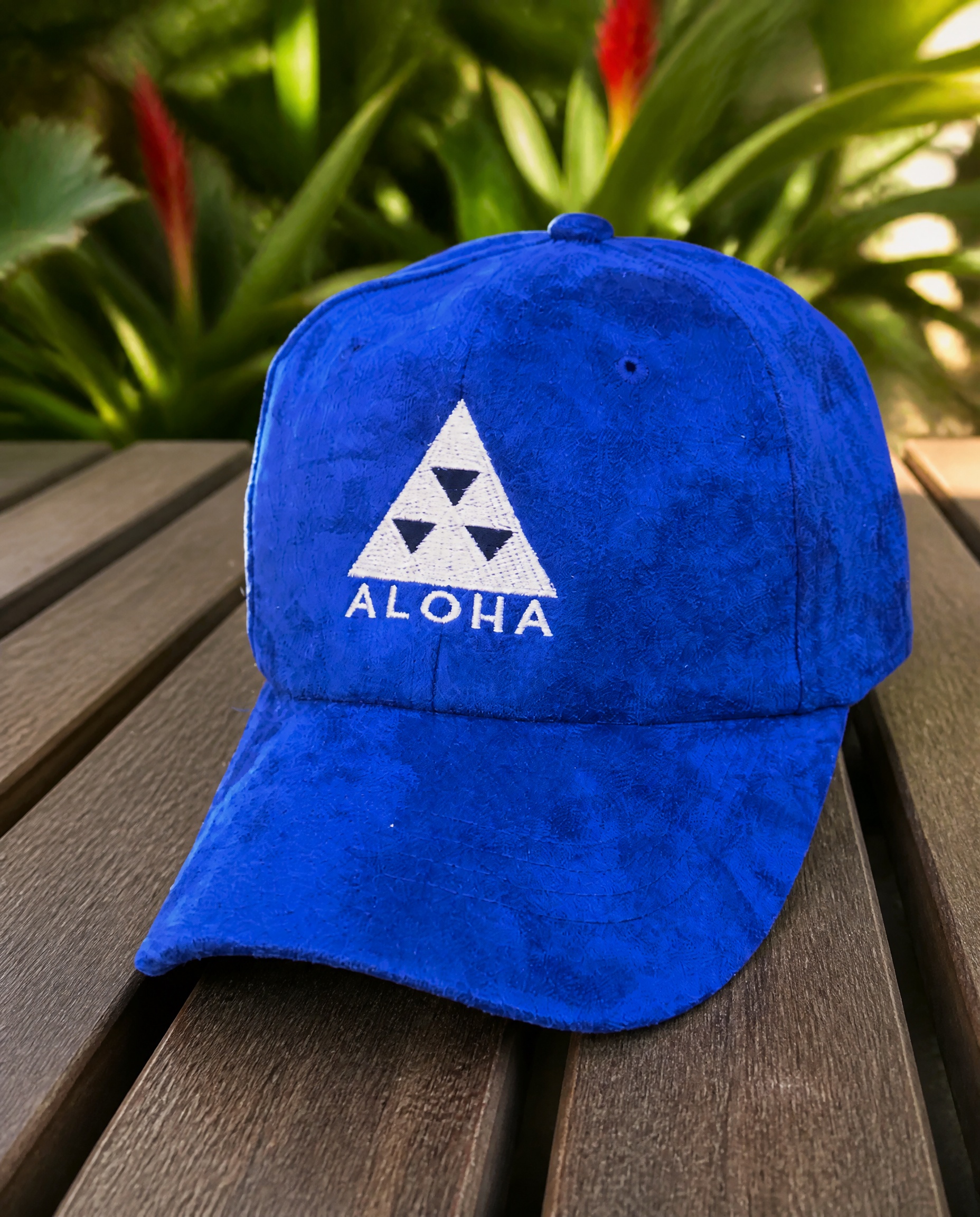 Blue Aloha logo baseball cap photographed on a tropical garden table