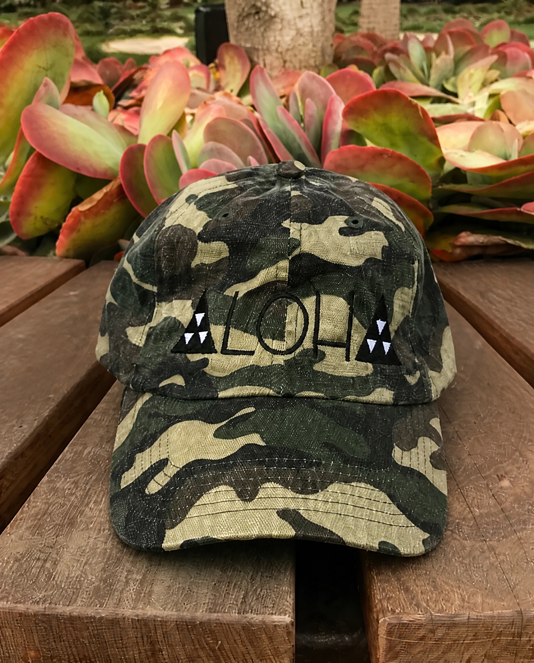 Black and olive camouflage Aloha cap photographed on a tropical garden table